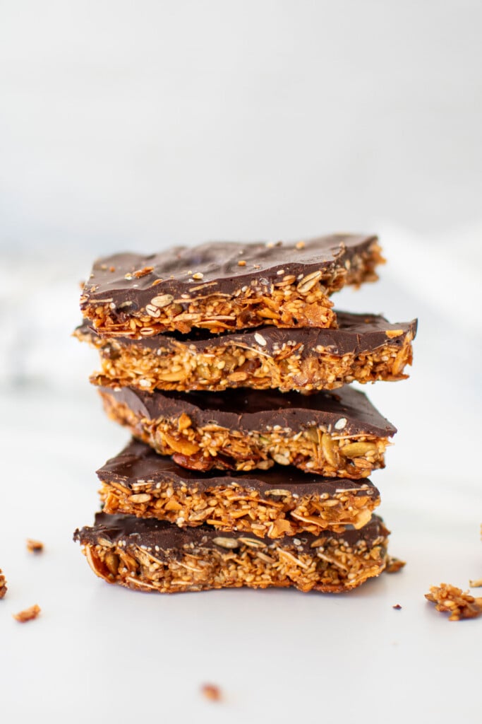 honey sesame dark chocolate bark pieces stacked on a white marble countertop.