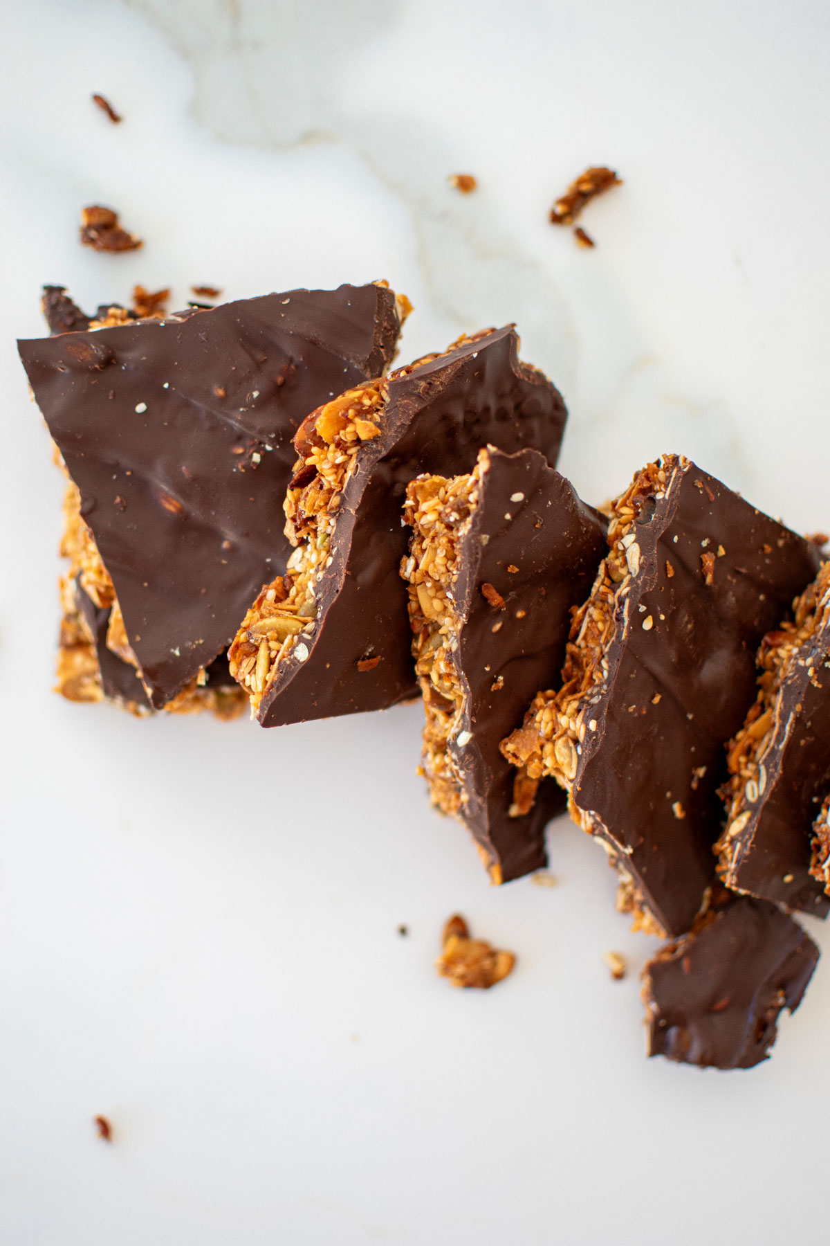 honey sesame dark chocolate bark pieces laid out on a white marble countertop.