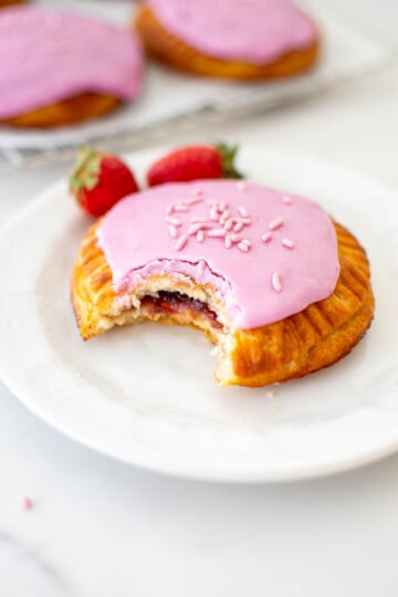 mixed berry hand pie with glaze with a bite taken out on a white dessert plate with fresh strawberries.