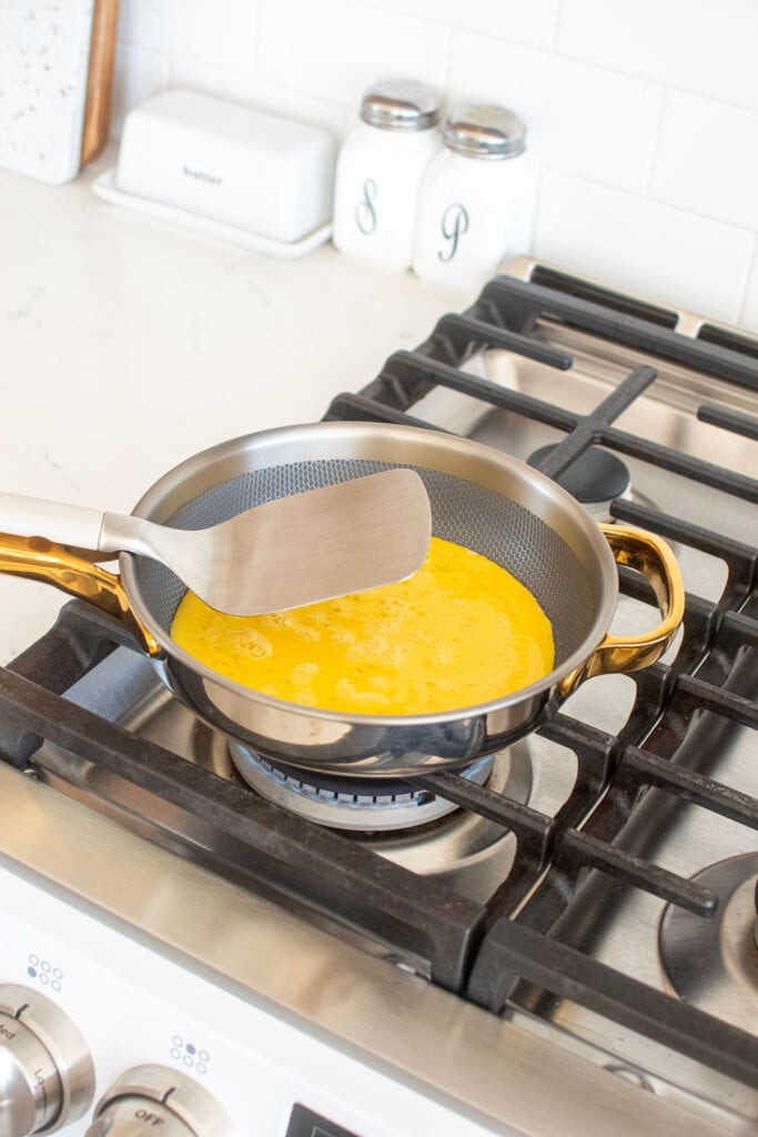 scrambled eggs being cooked in an our place titanium pan on the stovetop.