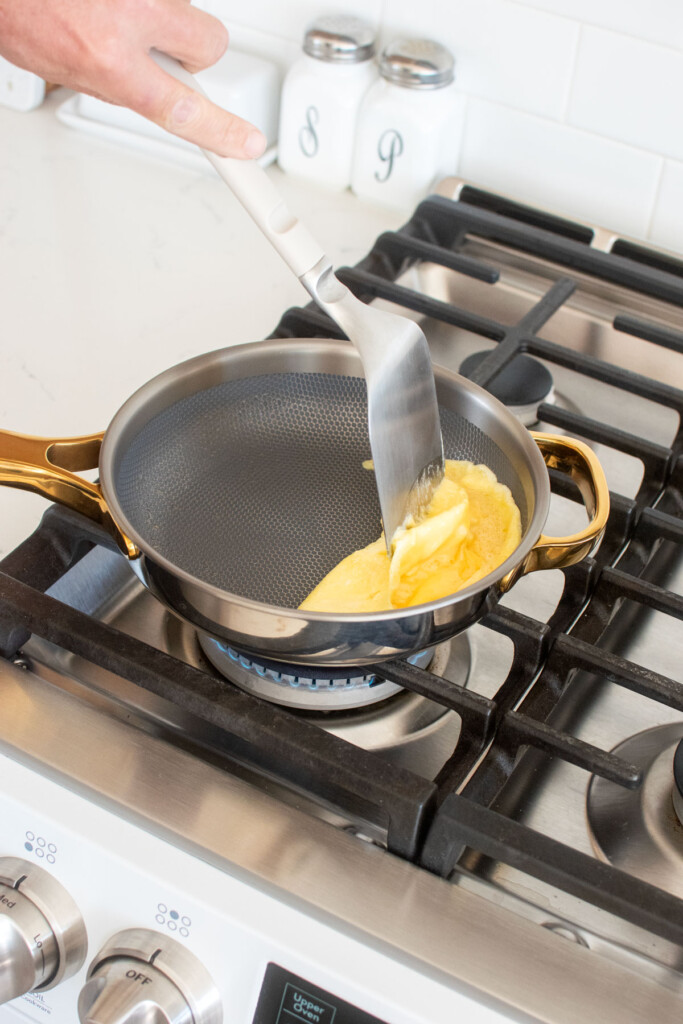 scrambled eggs being cooked in an our place titanium pan on the stovetop.