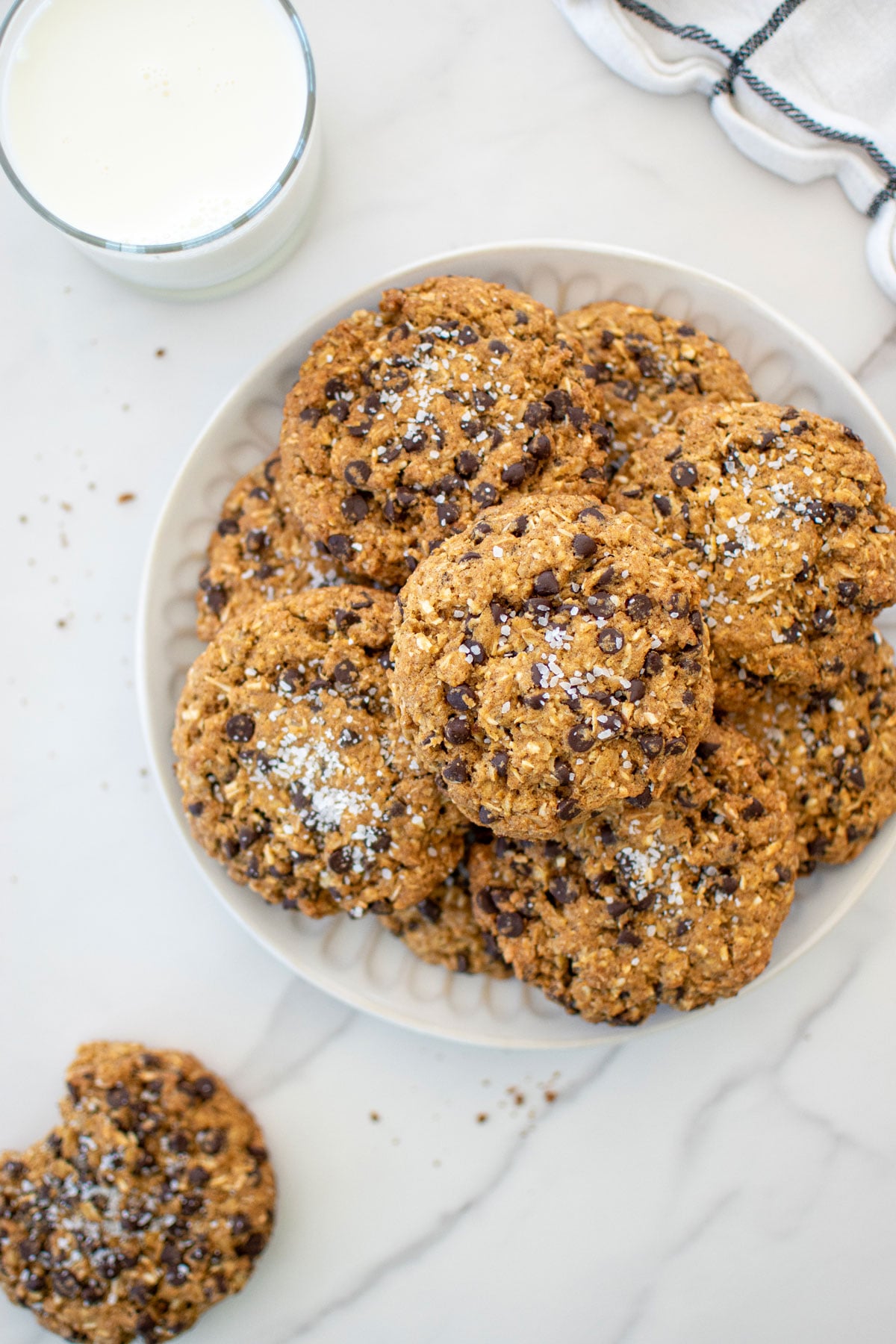 a plate of pumpkin oatmeal chocolate chip cookies on a white marble countertop with a glass of milk.
