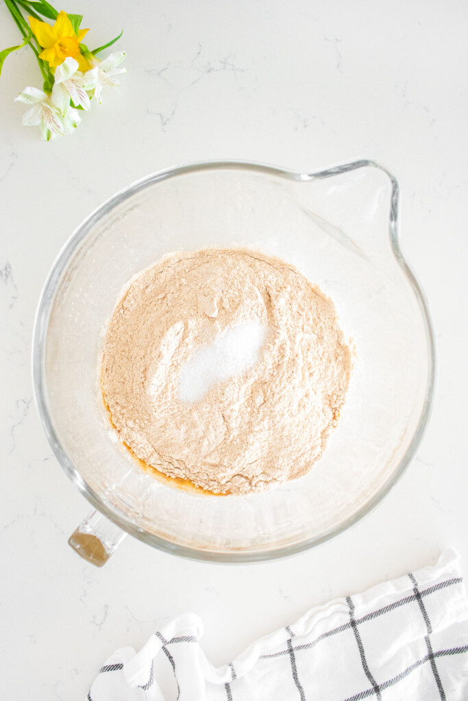 ingredients for sourdough discard whole wheat sandwich bread in a glass mixing bowl on a white marble counter.