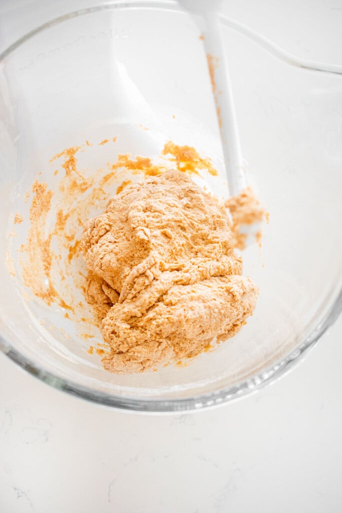 glass stand mixing bowl with sourdough discard whole wheat sandwich bread dough mixed until shaggy on a white marble counter.