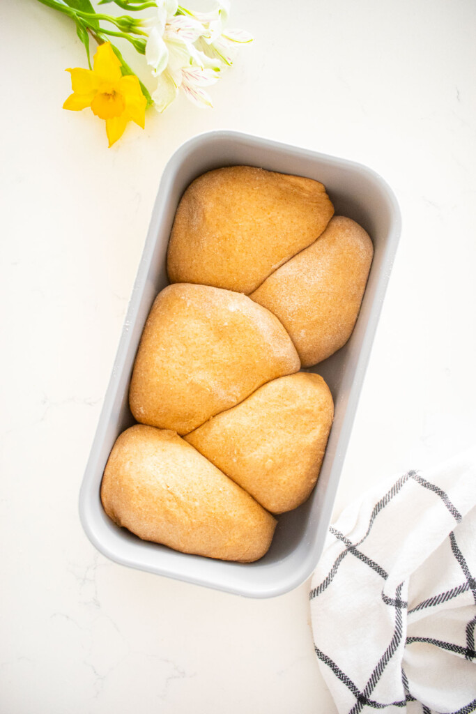 1-pound loaf pan with dough balls placed zig zag inside it on a white marble counter.