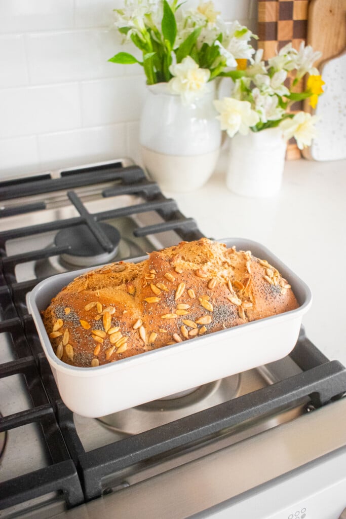 baked sourdough discard whole wheat sandwich bread in a loaf pan cooling on top of an oven.