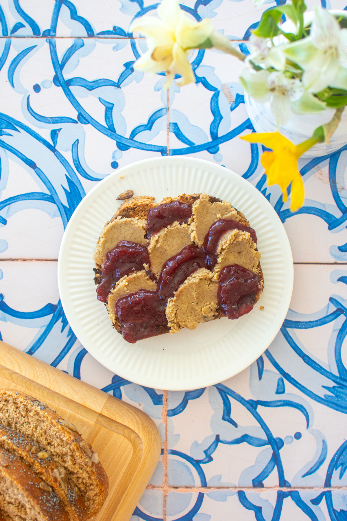 sourdough discard whole wheat sandwich bread toasted with cherry jam and walnut butter on a small plate on a blue tile table.