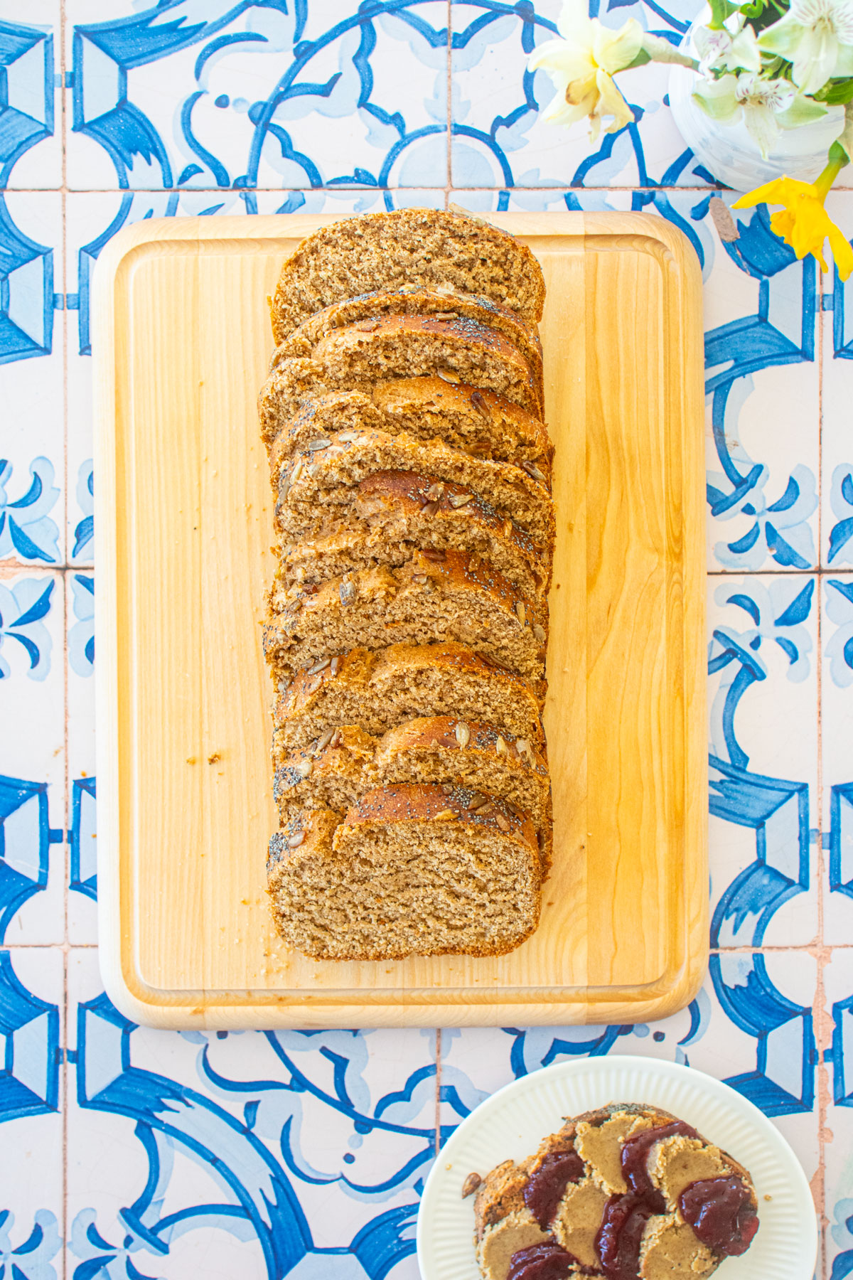 sourdough discard whole wheat sandwich bread sliced on a wood cutting board on a blue tile table with flowers.