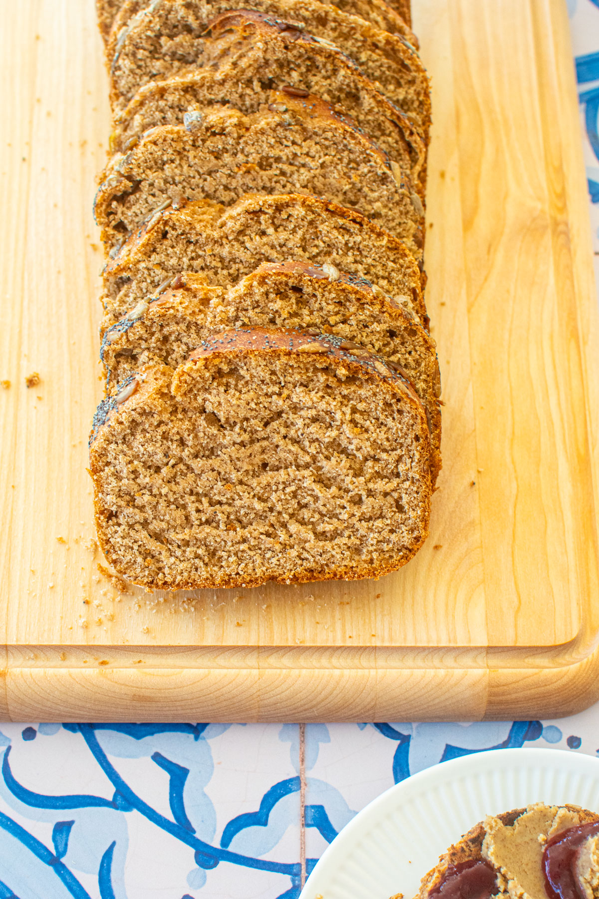 sourdough discard whole wheat sandwich bread sliced on a wood cutting board on a blue tile table.