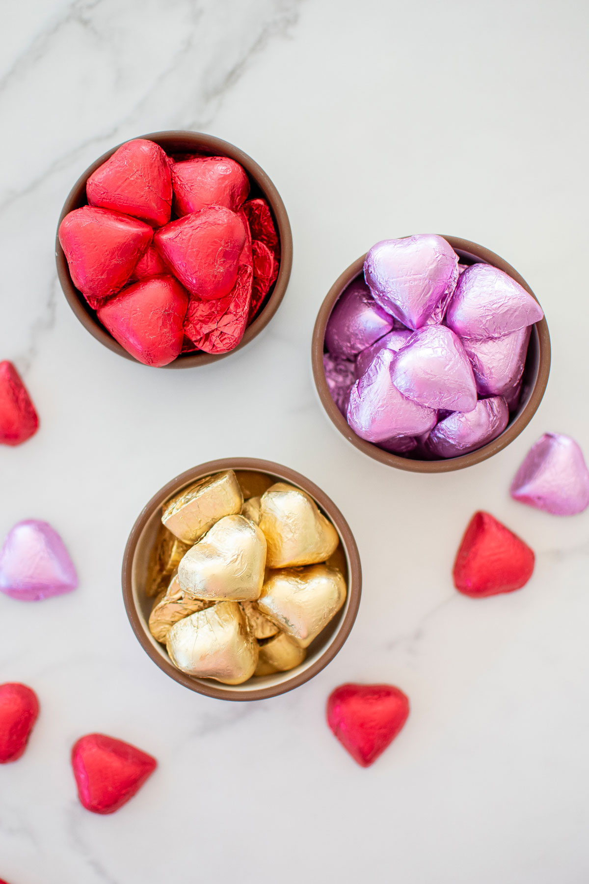 red, pink and gold wrapped foil hearts in small bowls on a white marble counter.