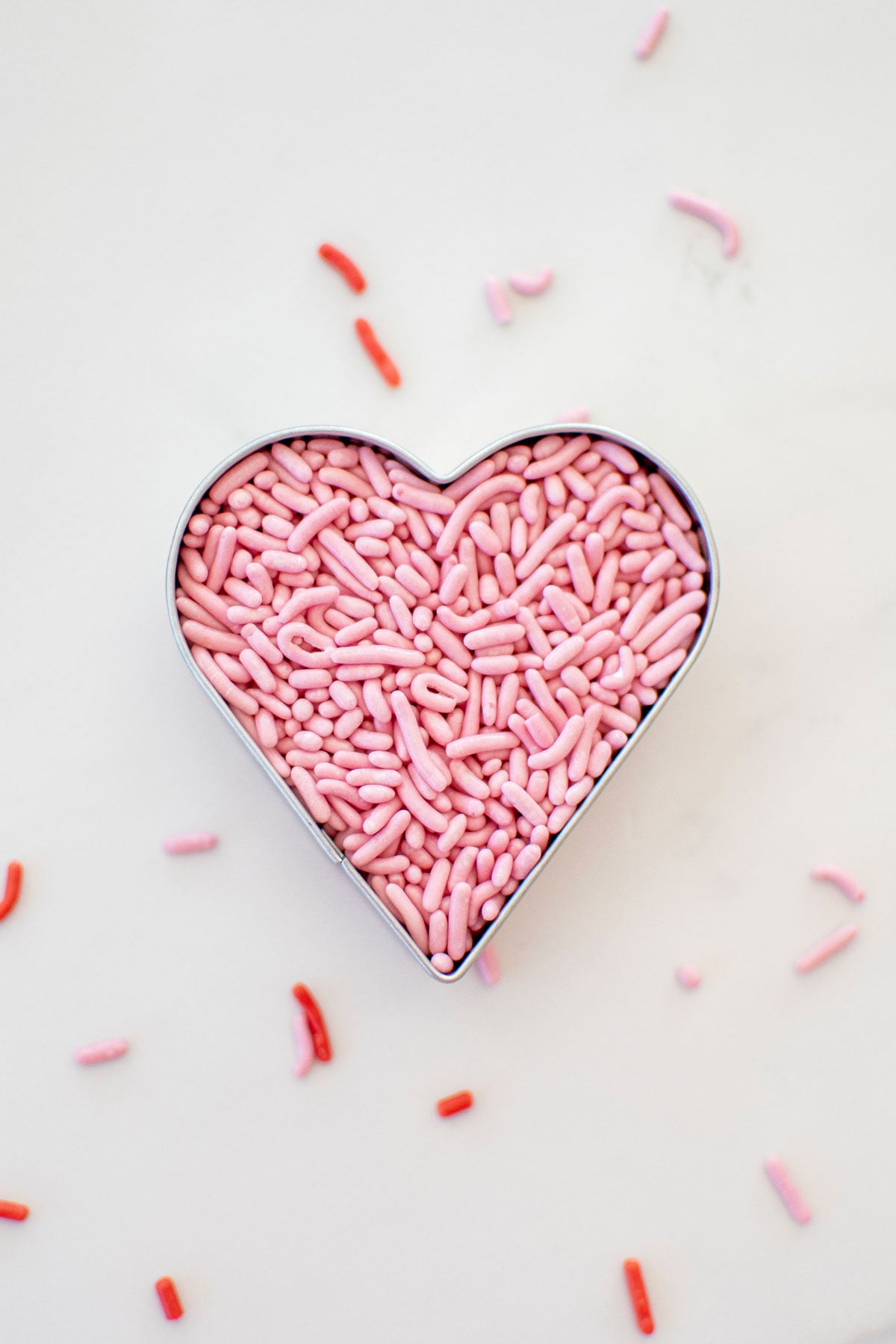pink sprinkles in a heart cookie cutter on a white marble counter.