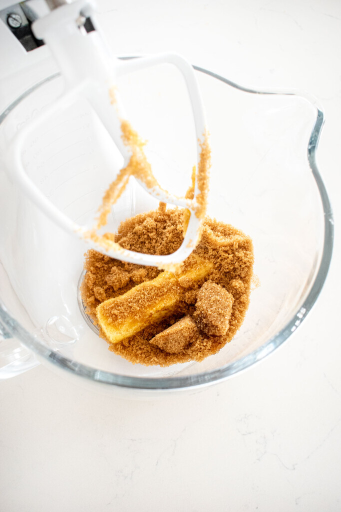butter and brown sugar in a glass stand mixing bowl on a white marble counter.