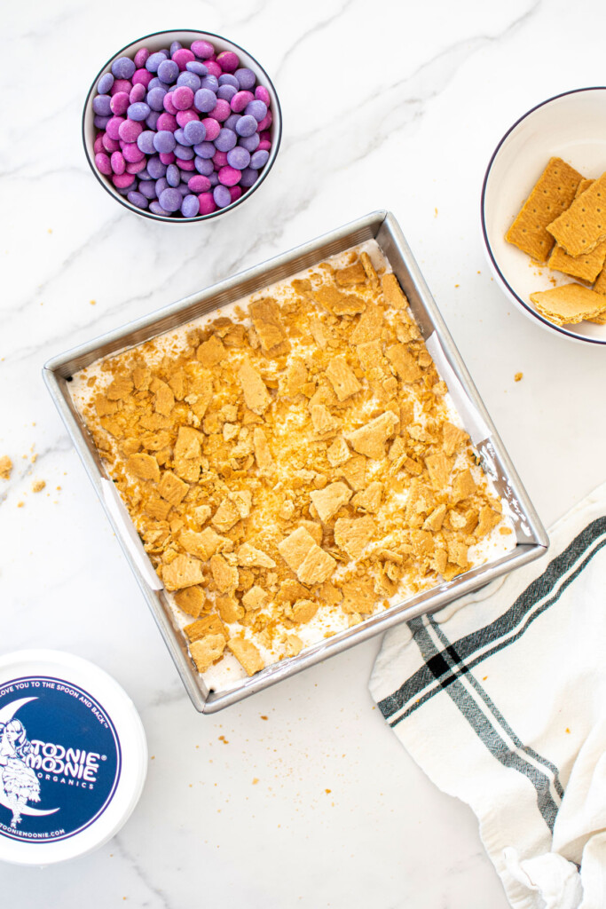 crushed up graham crackers on top of smore bars in a baking pan on white marble counter.