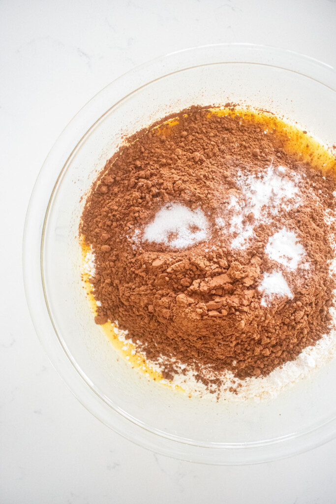 ingredients for chocolate cupcakes in a glass mixing bowl on a white marble counter.
