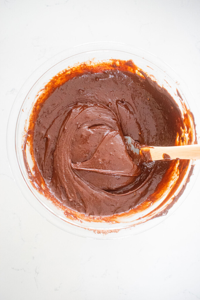 chocolate cupcake batter in a glass mixing bowl with a spatula on a white marble counter.