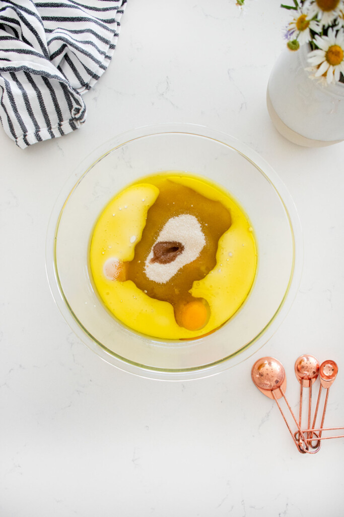 glass mixing bowl with wet ingredients for chocolate cupcakes on a marble counter with fresh flowers.
