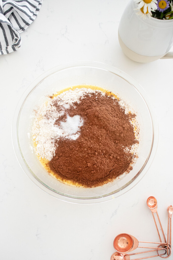 dry ingredients for chocolate cupcake batter being added to glass mixing bowl on a marble counter.
