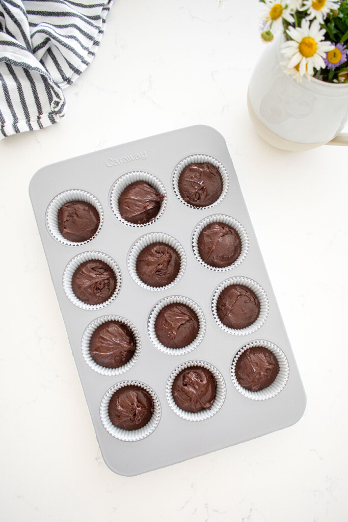 cupcake tray with chocolate cupcake batter in it on a marble counter with fresh flowers.