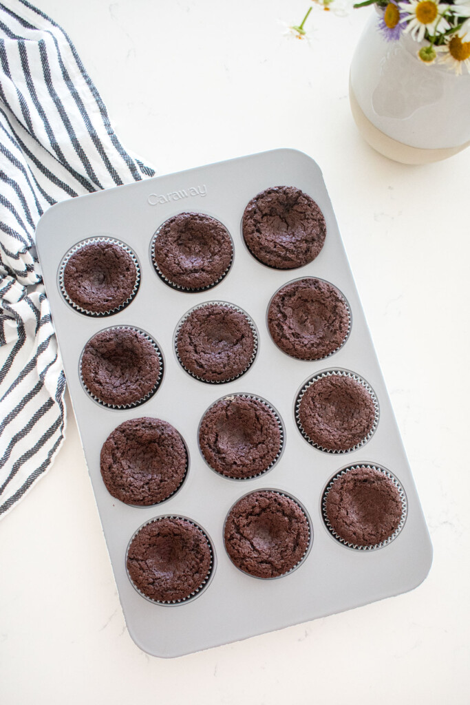 baked chocolate cupcakes in a cupcake pan on a marble counter with fresh flowers.