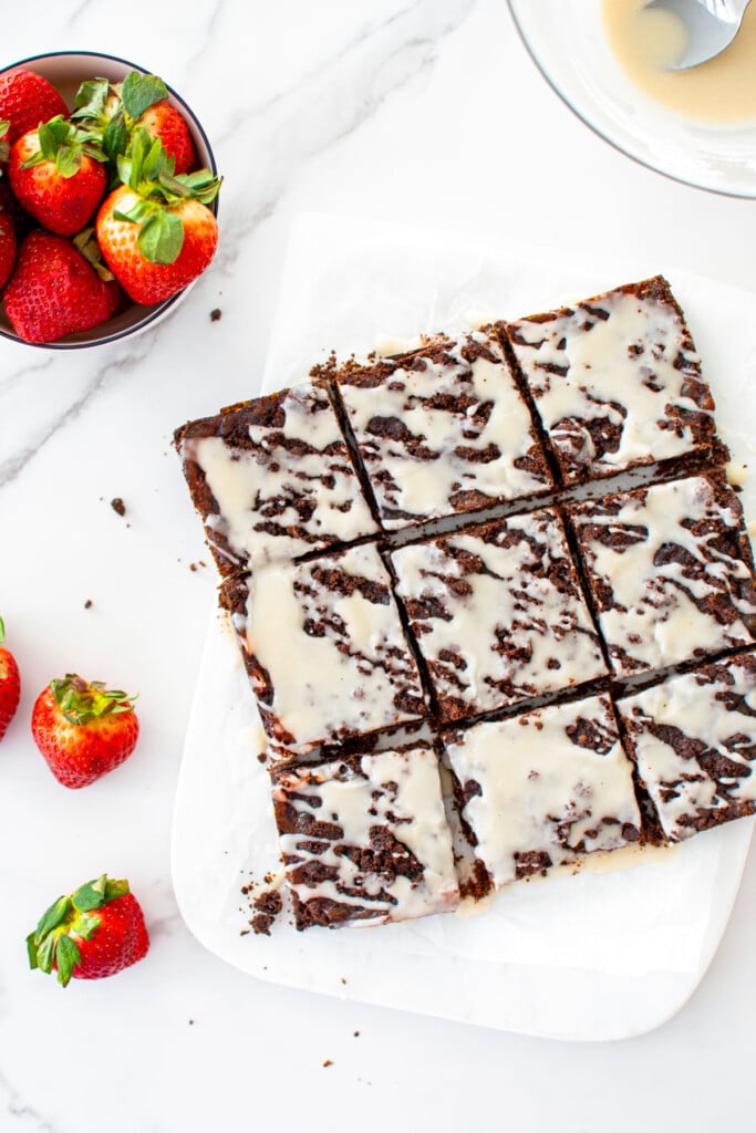 chocolate strawberry crumb bars cut into squares with fresh strawberries on a white marble counter.