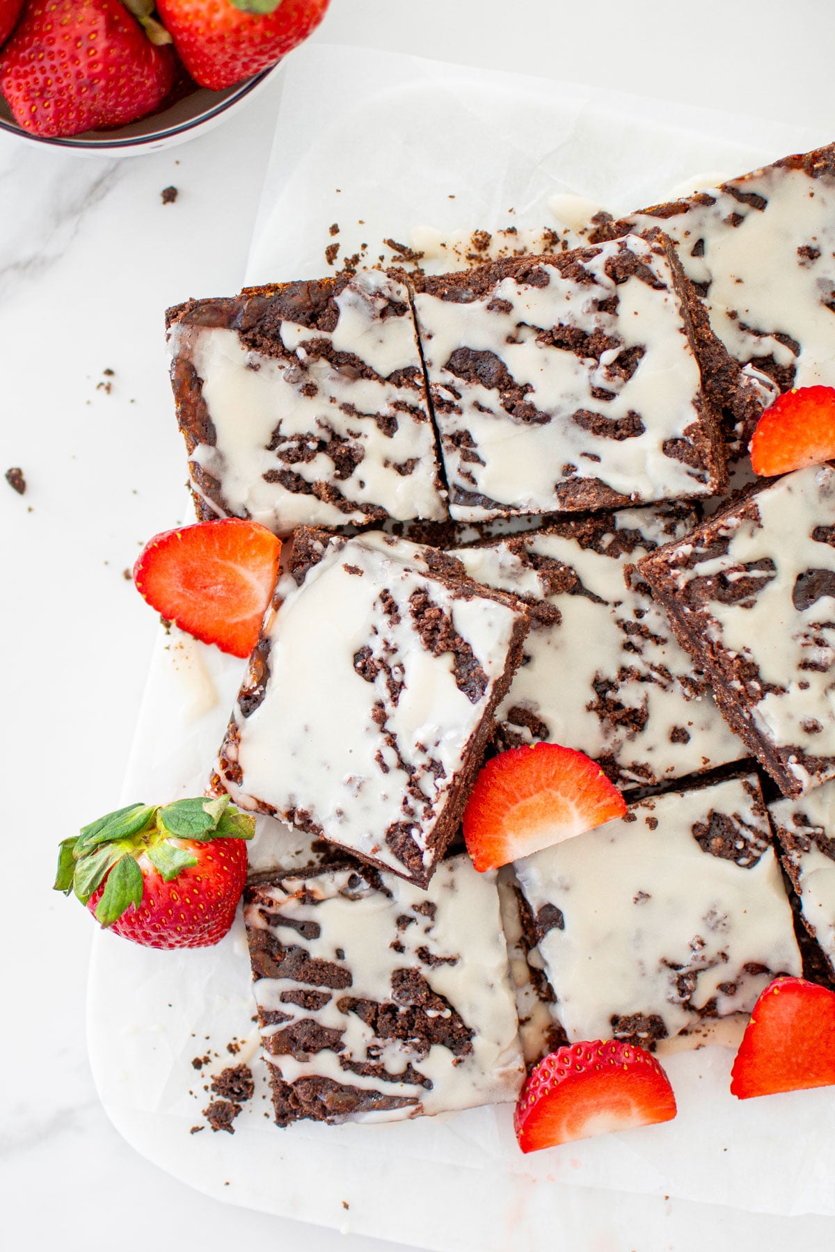 chocolate strawberry crumb bars cut into squares with fresh strawberries on a white marble counter.