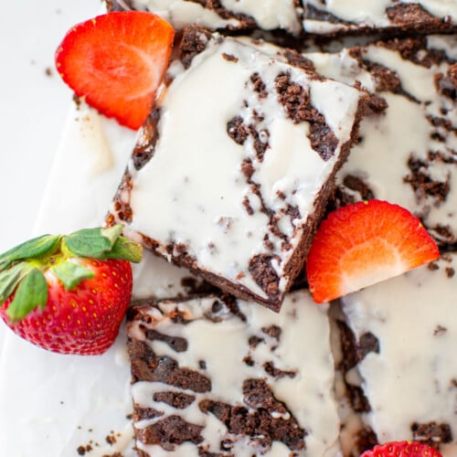 chocolate strawberry crumb bars cut into squares with fresh strawberries on a white marble counter.