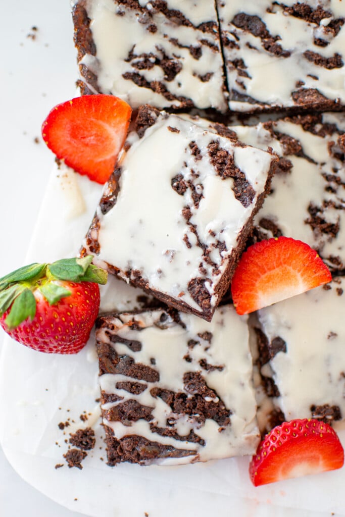 chocolate strawberry crumb bars cut into squares with fresh strawberries on a white marble counter.