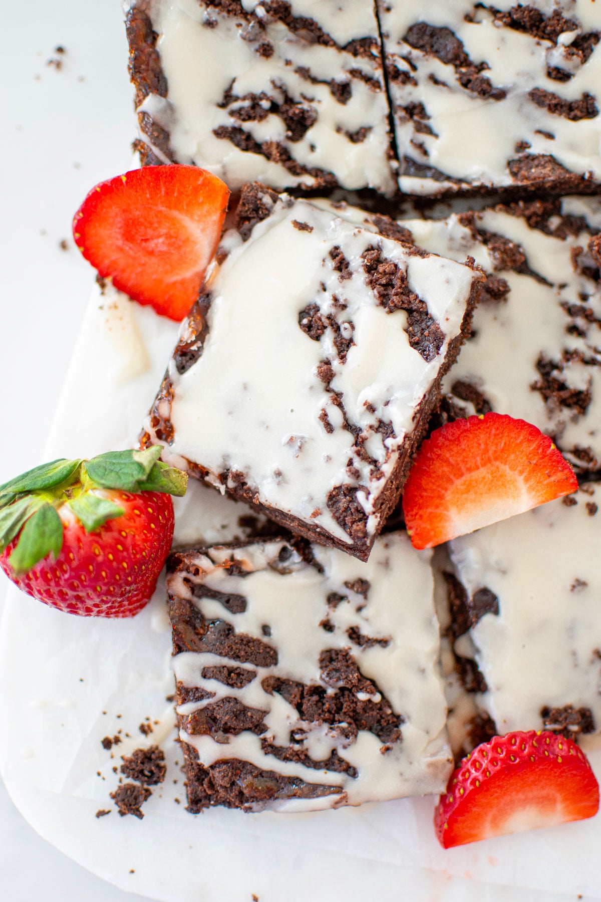 chocolate strawberry crumb bars cut into squares with fresh strawberries on a white marble counter.