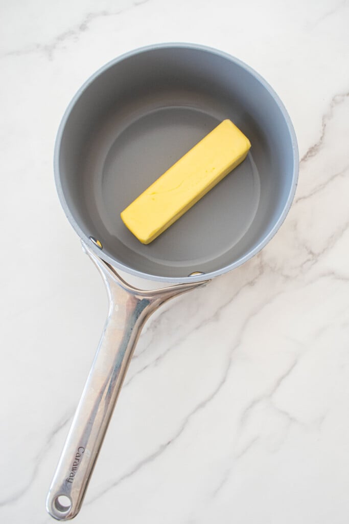 stick of butter in a small pot on a white marble counter.