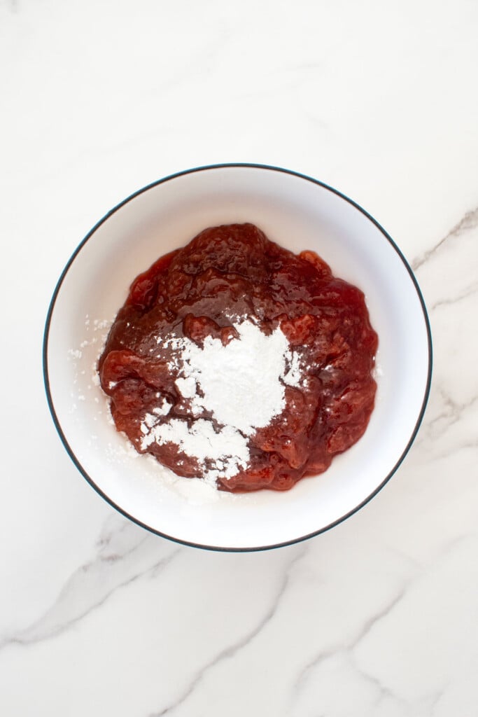 strawberry jam with cornstarch in a white bowl on a white marble counter.