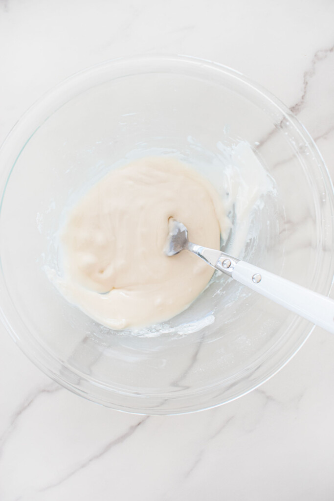 glaze in a glass mixing bowl on a white marble counter.
