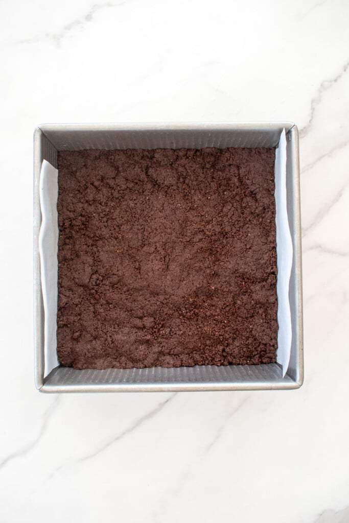 baked chocolate shortbread cookie dough base in a square baking pan on a white marble counter.