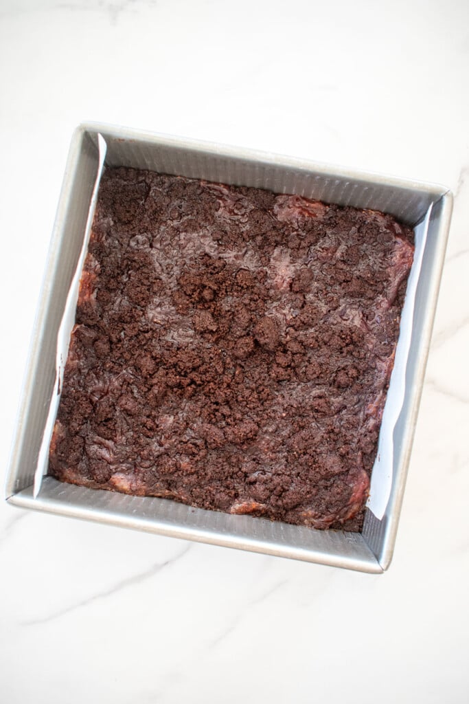 baked chocolate strawberry crumb bars in a square baking pan on a white marble counter.