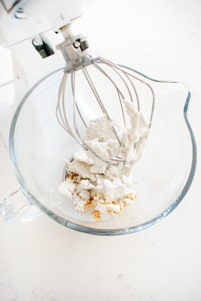 ingredients for vegan whipped cream in a glass mixing bowl on a marble counter.