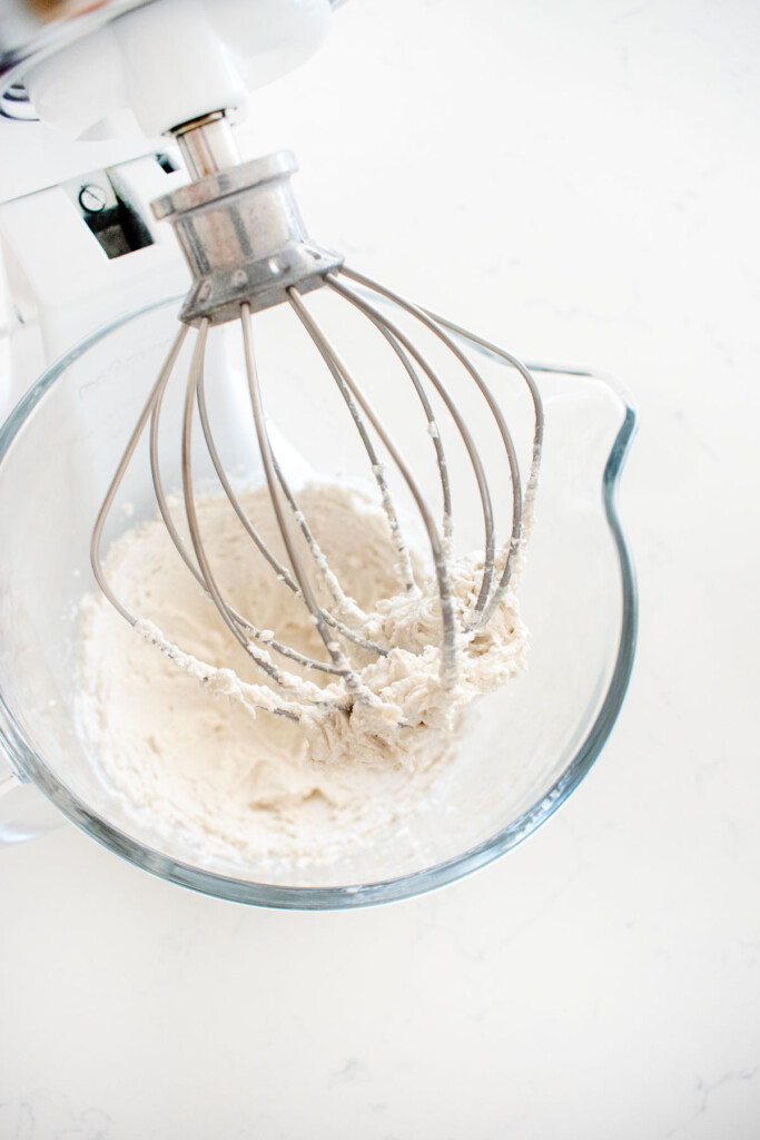 vegan whipped cream in a glass mixing bowl on a marble counter.