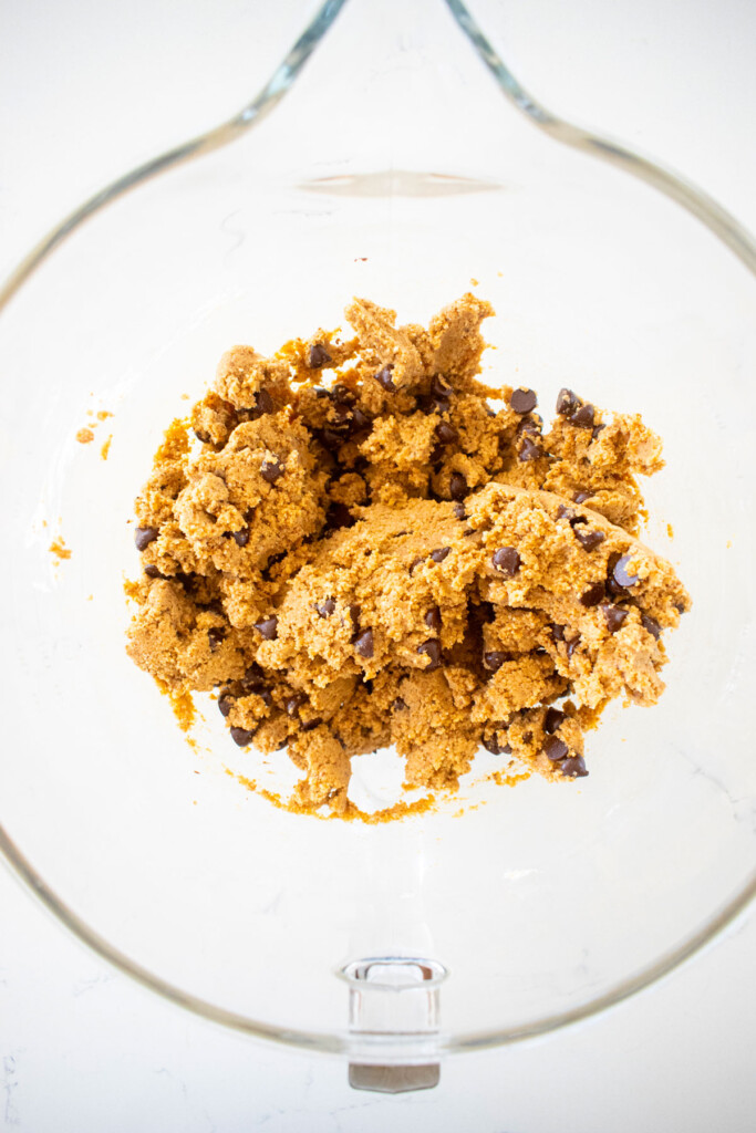 healthy chocolate chip cookie dough in a glass mixing bowl on a marble counter.