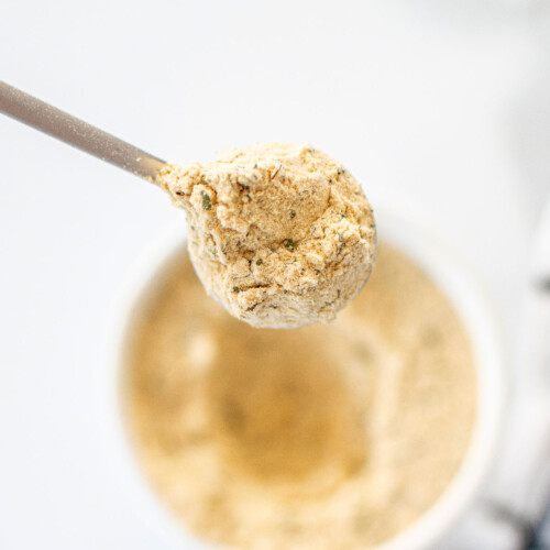 spoon of homemade ranch seasoning coming out of a bowl on a white marble countertop.