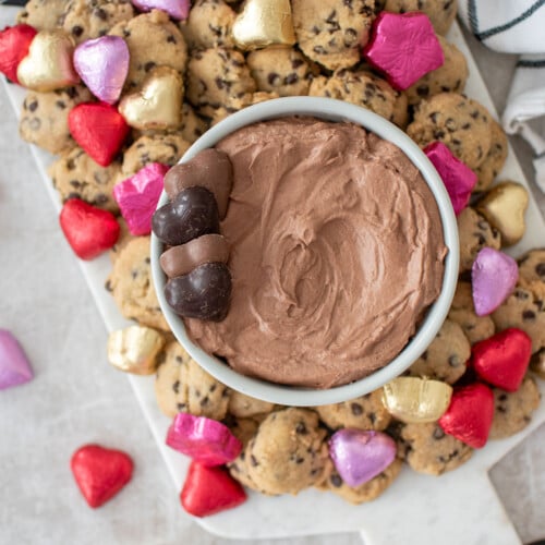hot chocolate dip in a bowl on a board with mini chocolate chip cookies and chocolate hearts.