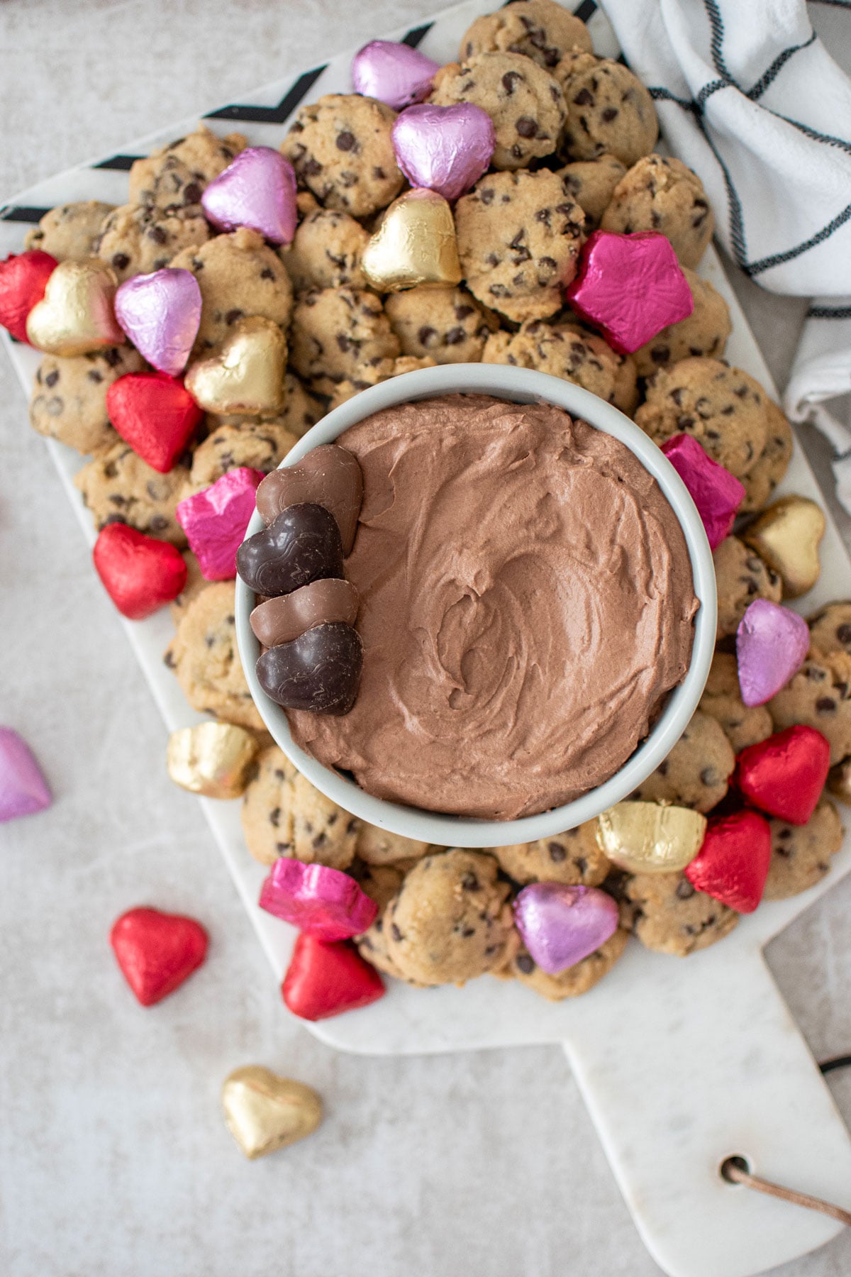 hot chocolate dip in a bowl on a board with mini chocolate chip cookies and chocolate hearts.