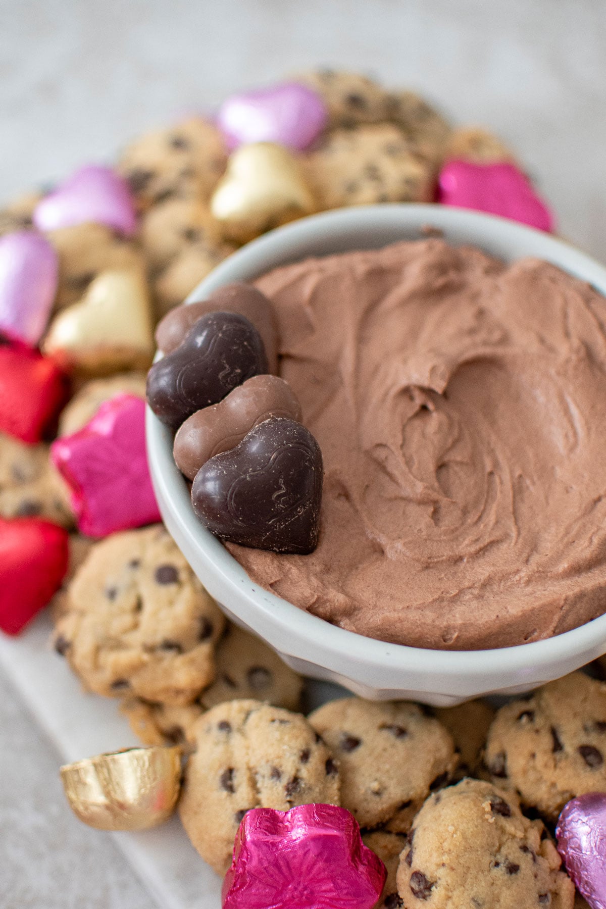 hot chocolate dip in a bowl on a board with mini chocolate chip cookies and chocolate hearts.