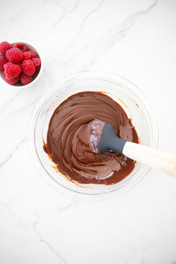 chocolate ganache in a glass mixing bowl on a white marble countertop.