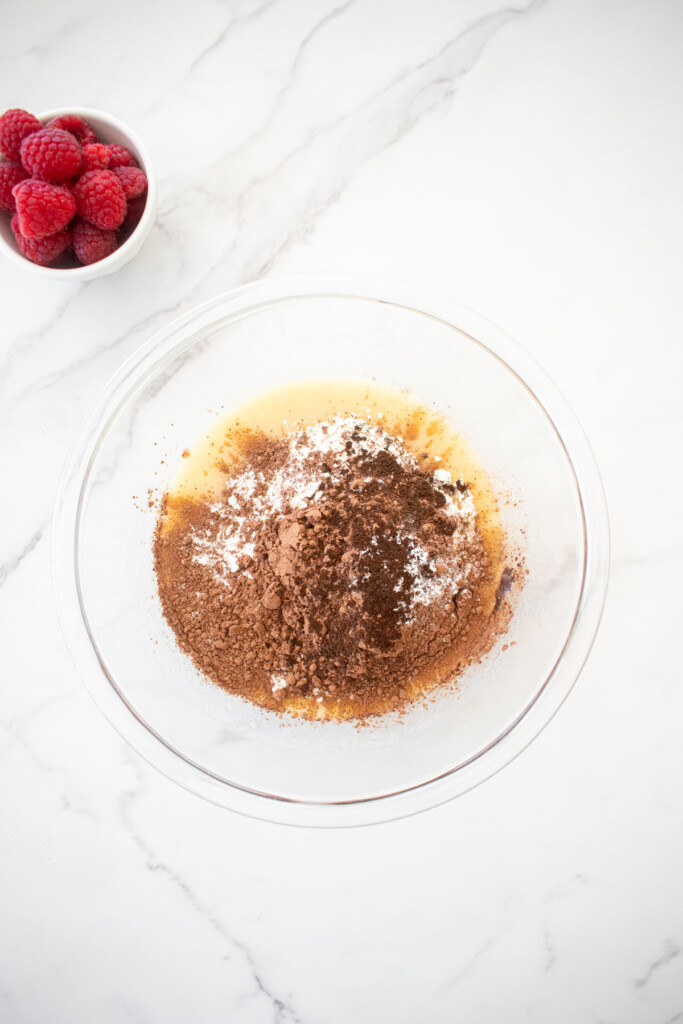 ingredients for small batch chocolate cake with sourdough discard in a glass mixing bowl on a white marble countertop.