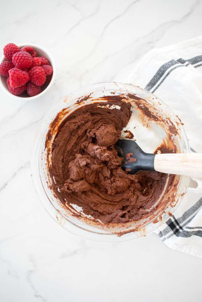 whipped chocolate ganache in a glass mixing bowl on a white marble countertop.