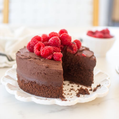 small batch chocolate cake with sourdough discard topped with fresh raspberries on a plate on plate with a slice cut out.