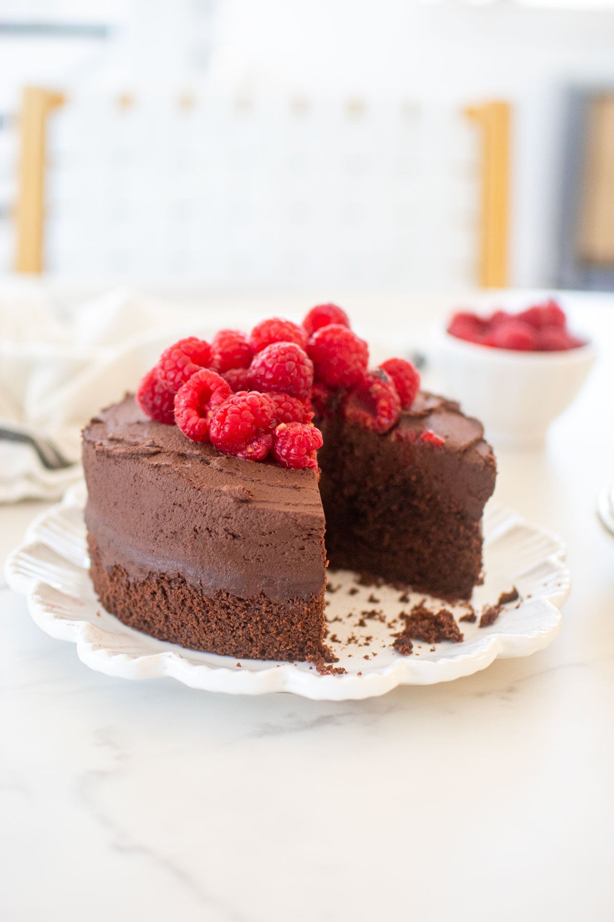 small batch chocolate cake with sourdough discard topped with fresh raspberries on a plate on plate with a slice cut out.