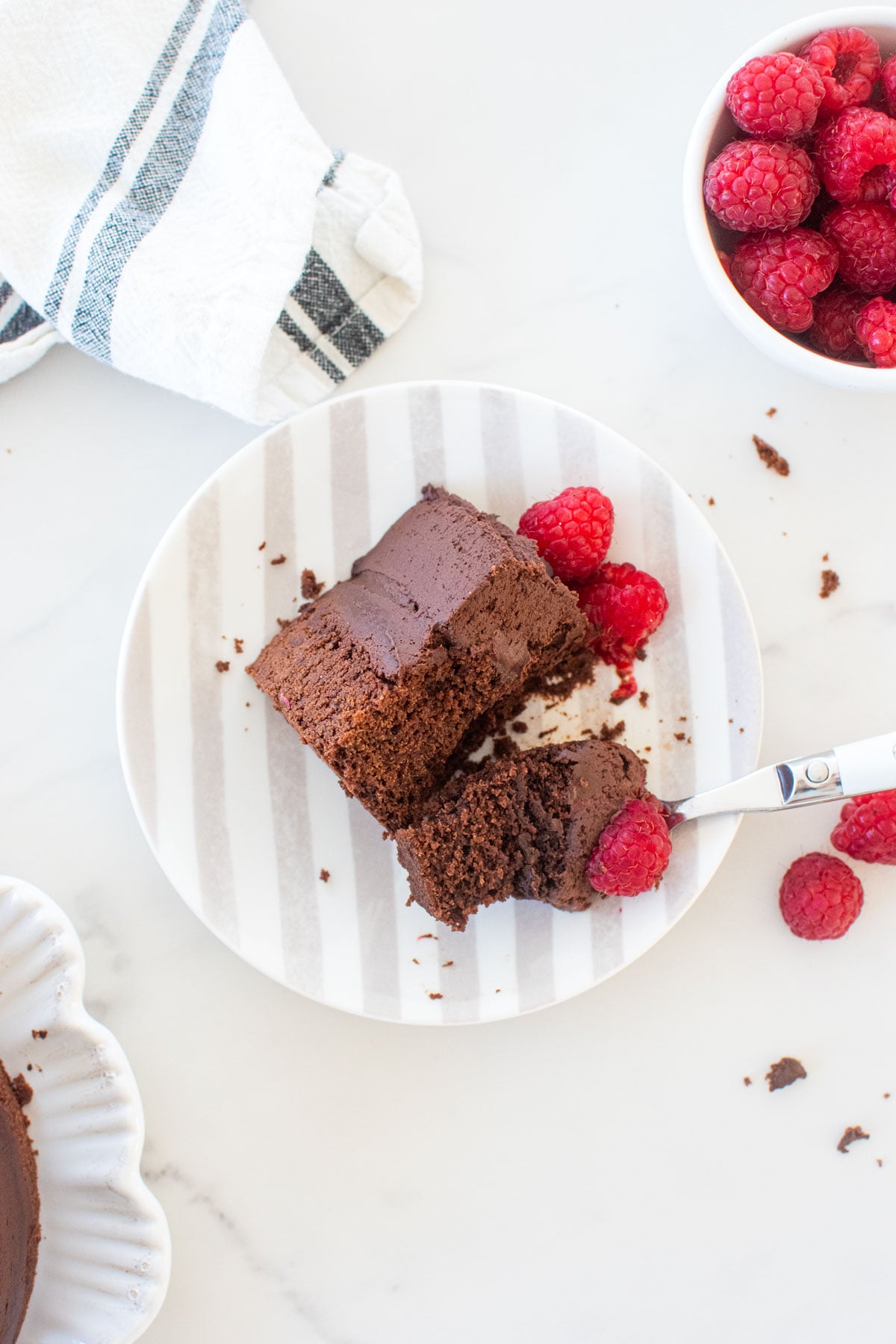 slice of small batch chocolate cake with sourdough discard on a striped plate on a white marble countertop.