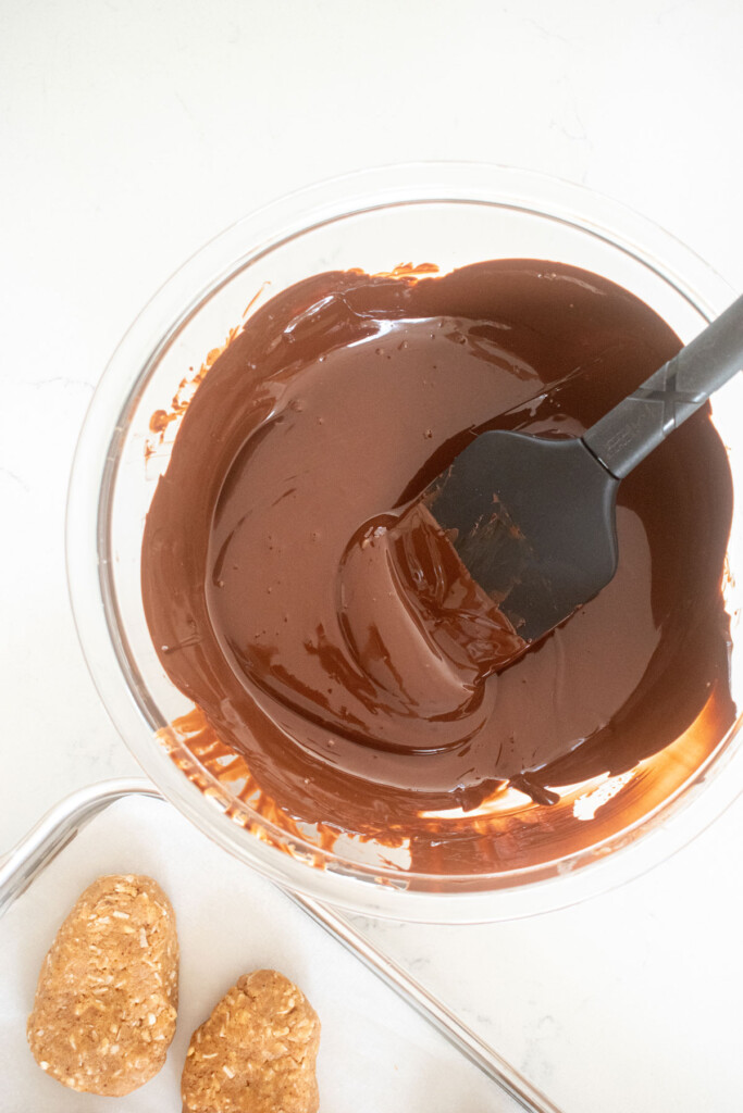 dark chocolate melted in a glass mixing bowl on a marble counter with a spatula in the bowl.