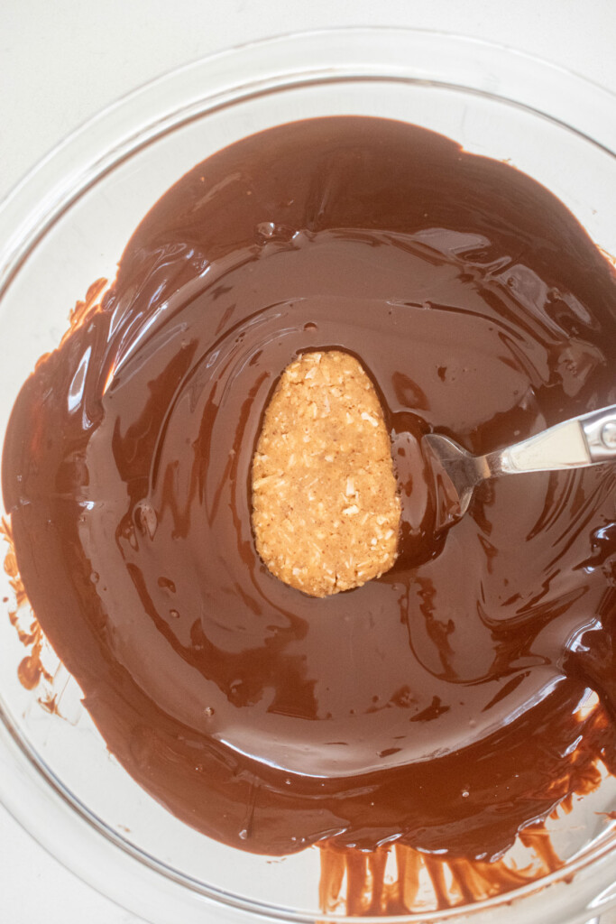 coconut almond butter egg being dipped into a bowl of melted dark chocolate.