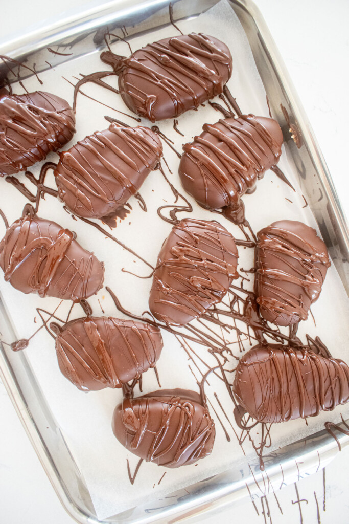 chocolate drizzled on top of dark chocolate coconut almond butter eggs on a baking sheet.