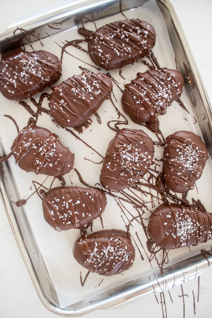 dark chocolate coconut almond butter eggs with flaky sea salt on a baking sheet on a marble counter.